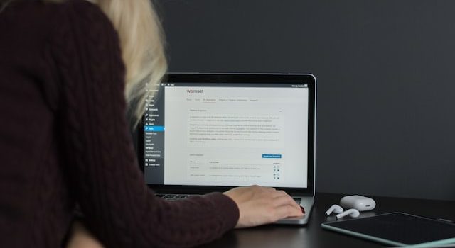 امرأة شقراء تجلس على مكتب وتعمل على جهاز كمبيوتر محمول