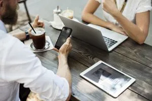 Dos personas sentadas en presencia de un teléfono, una PC y una tableta.