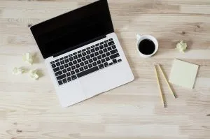 فنجان قهوة وقلام رصاص بجانب جهاز كمبيوتر محمول.
