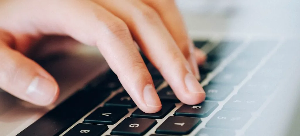 Osoba pisząca coś na klawiaturze laptopa.