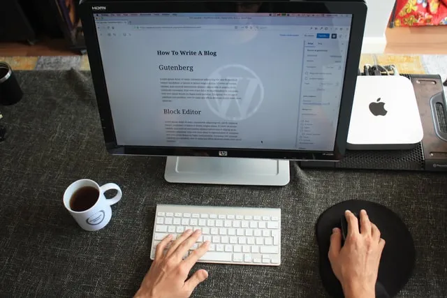 شخص جالس على مكتب الكمبيوتر وبجانبه كوب قهوة وفتح صفحة WordPress على الشاشة