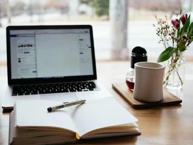 Sebuah notebook dan laptop di atas meja.