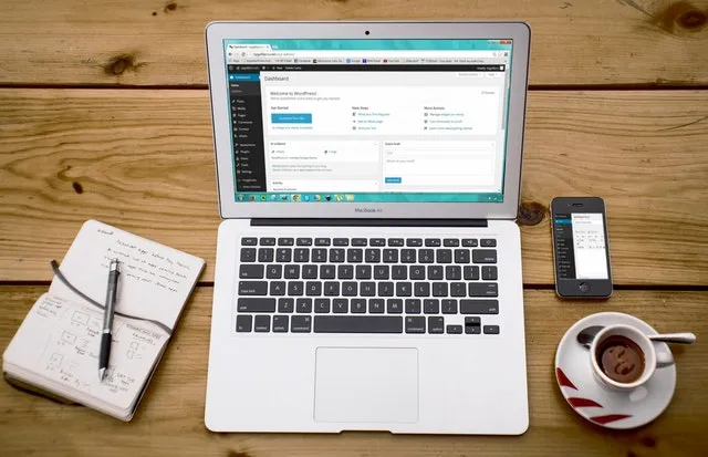 Un laptop con una pagina WordPress aperta su di esso con un blocco note su un lato e una tazza di caffè sull'altro