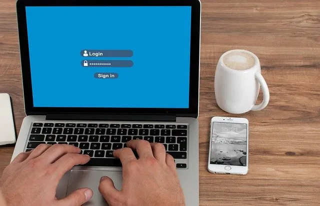 Una persona che digita i propri dati di accesso su un laptop posizionato accanto a una tazza bianca e uno smartphone