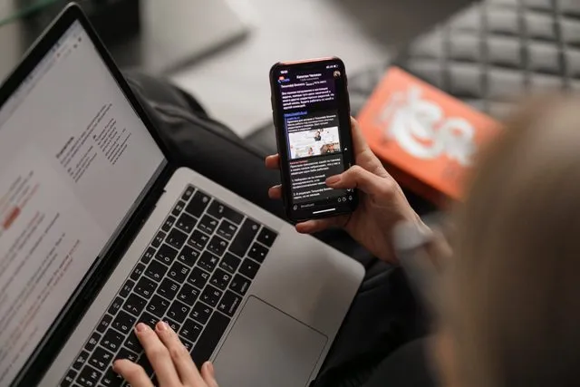 Una donna che usa il telefono e il laptop contemporaneamente.