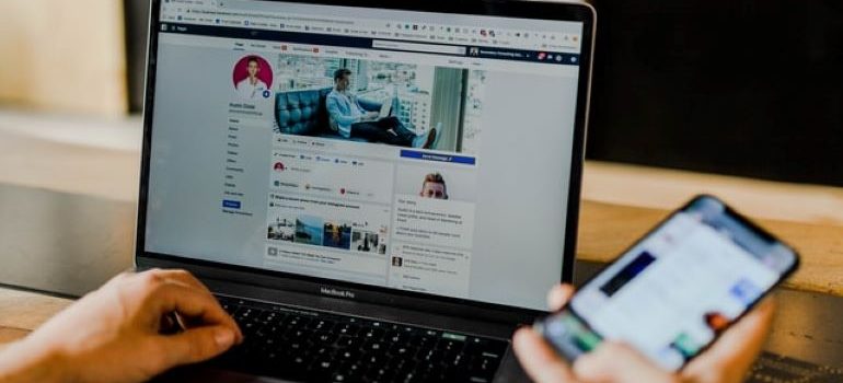 Facebook 페이지도 열려 있는 노트북 옆에 Facebook 앱이 열려 있는 휴대전화를 들고 있는 사람