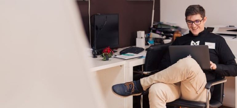 Pria yang duduk di kursi, melihat laptopnya dan tersenyum