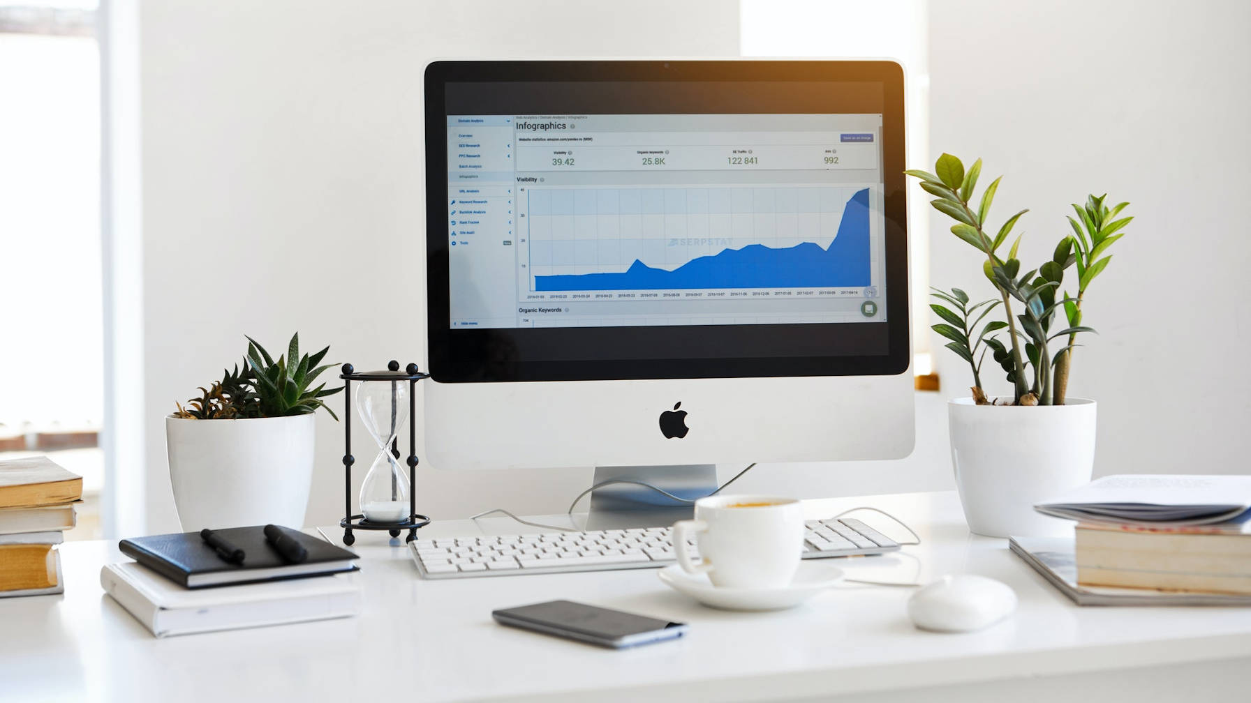 Декоративное изображение белого рабочего стола с ассортиментом предметов, включая компьютер Apple и кофейную кружку.