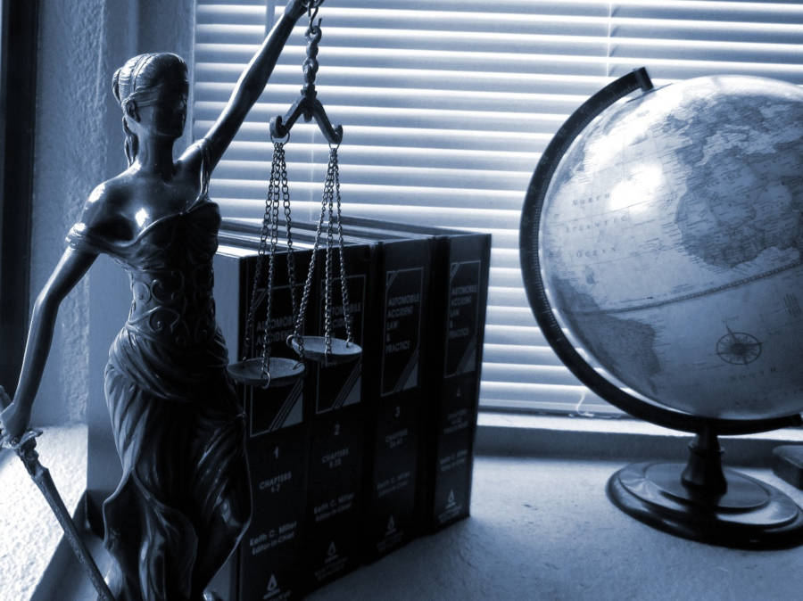 Lady Justice sentada em uma mesa com um fundo de livros e um globo.