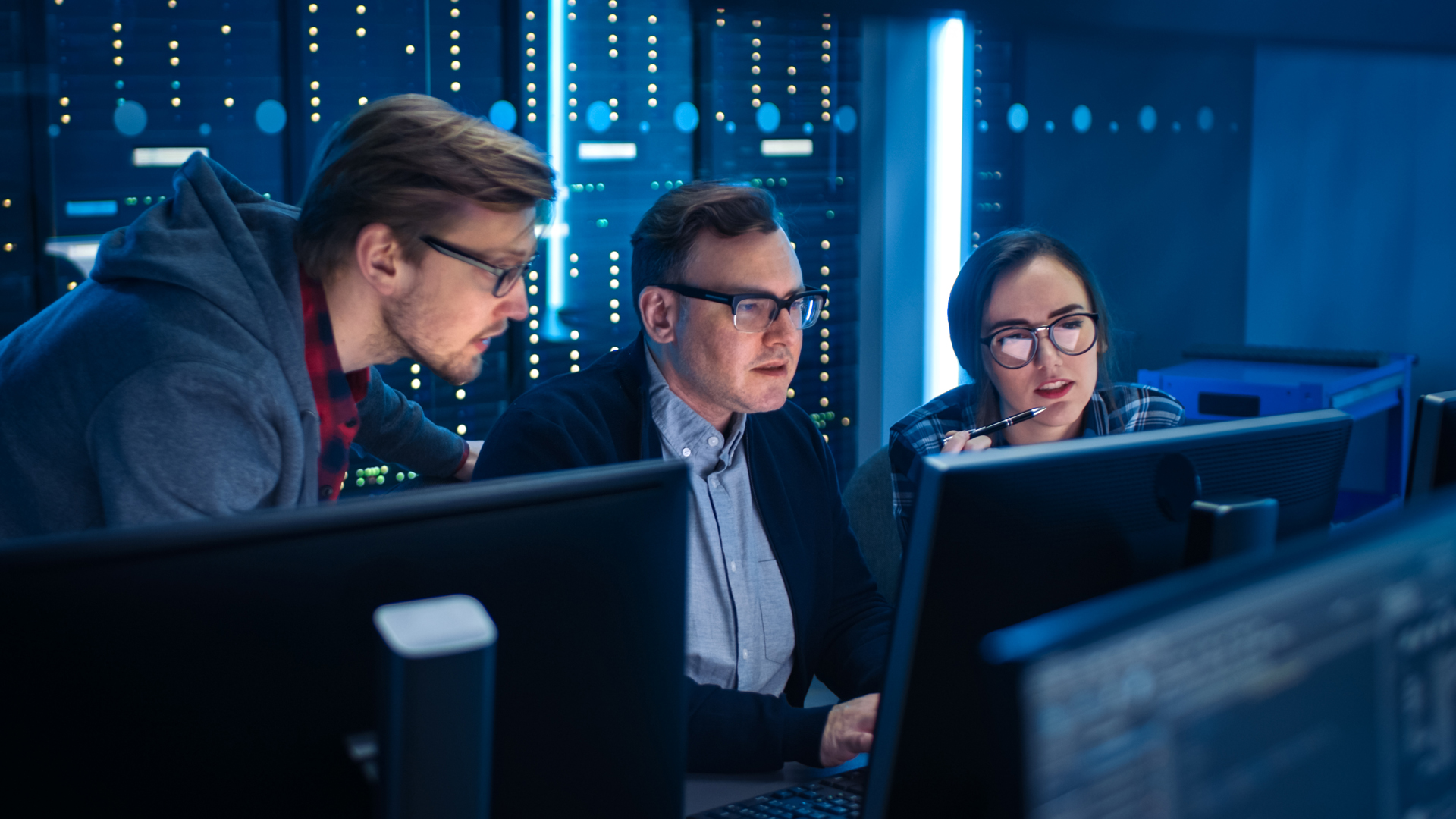 Drei Kollegen arbeiten an Computern vor dem Serverraum