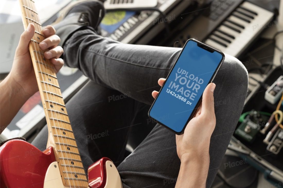 一个男人一边弹吉他一边看着他的 iphone xs max 的模型
