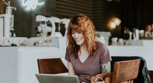 Seorang wanita tersenyum saat mengerjakan laptopnya.