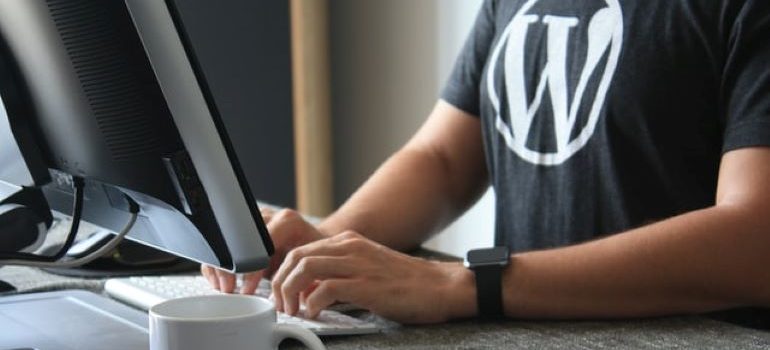 Orang dengan T-shirt dengan logo WordPress di atasnya mengetik sesuatu di keyboard