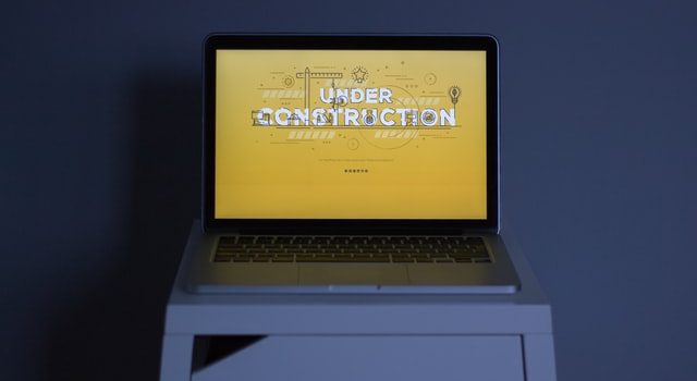 Laptop dengan halaman kuning yang bertuliskan sedang dibangun di atas meja putih
